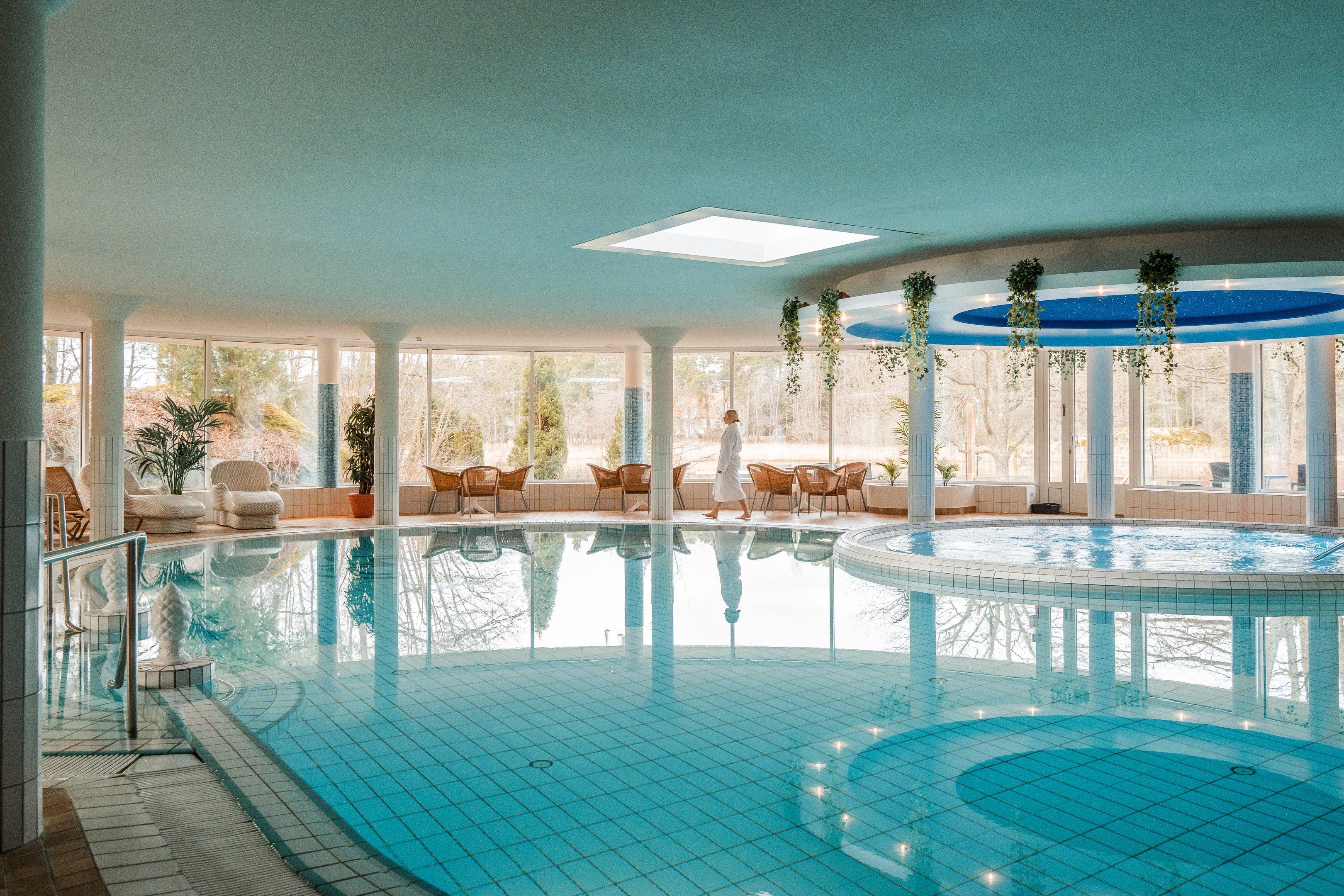 Sisäuima-allas porealtaalla, suuret ikkunat ja henkilö valkoisessa kylpytakissa.
