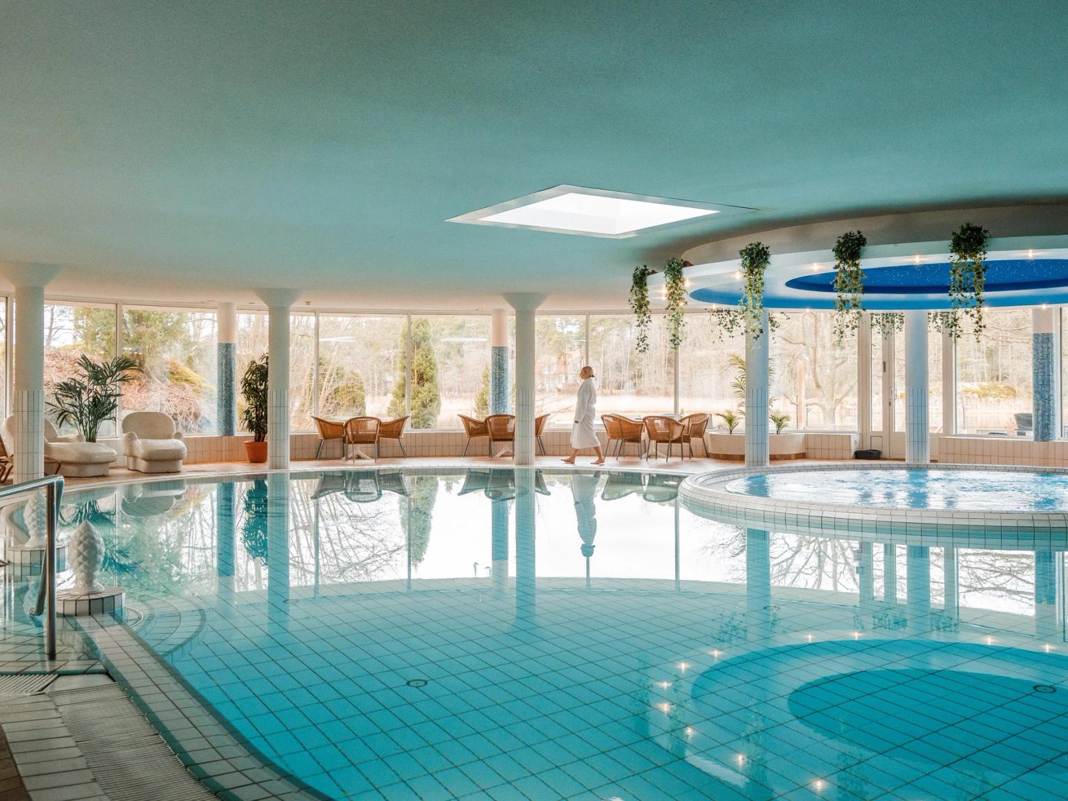 Sisäuima-allas porealtaalla, suuret ikkunat ja henkilö valkoisessa kylpytakissa.