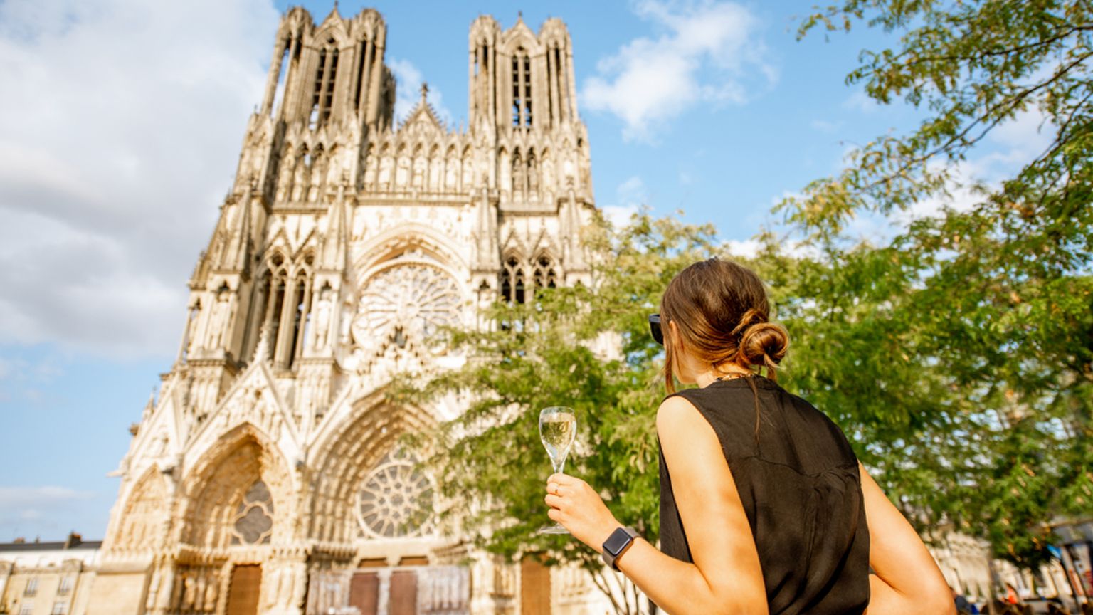 Mujer sosteniendo champán y contemplando la catedral de Reims.