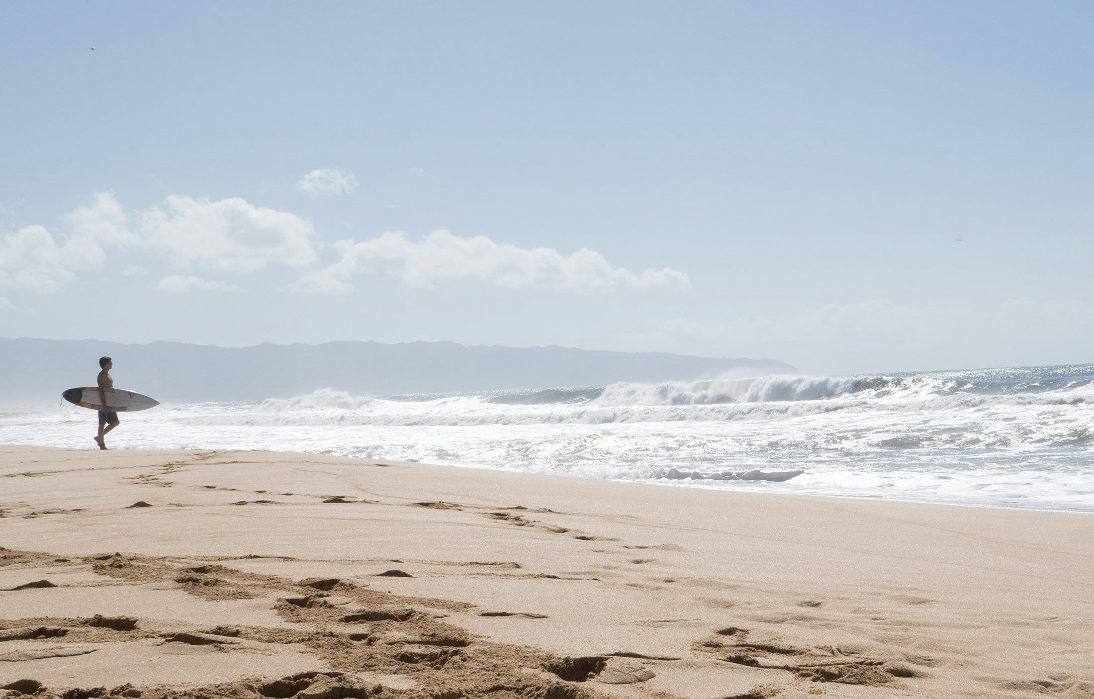 a man is walking on the beach carrying a surfboard
