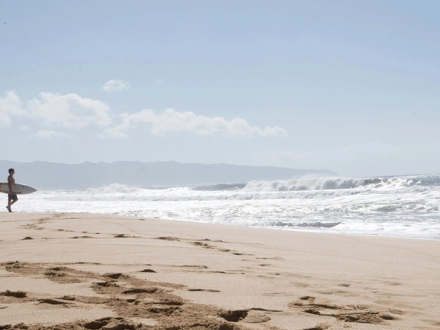 a man is walking on the beach carrying a surfboard