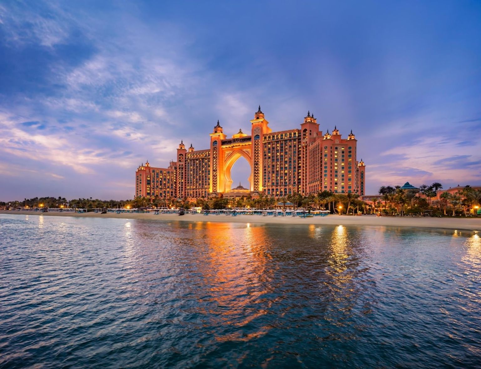 Opplyst Atlantis, The Palm hotell i skumringen, reflekterende i vannet med en strand.