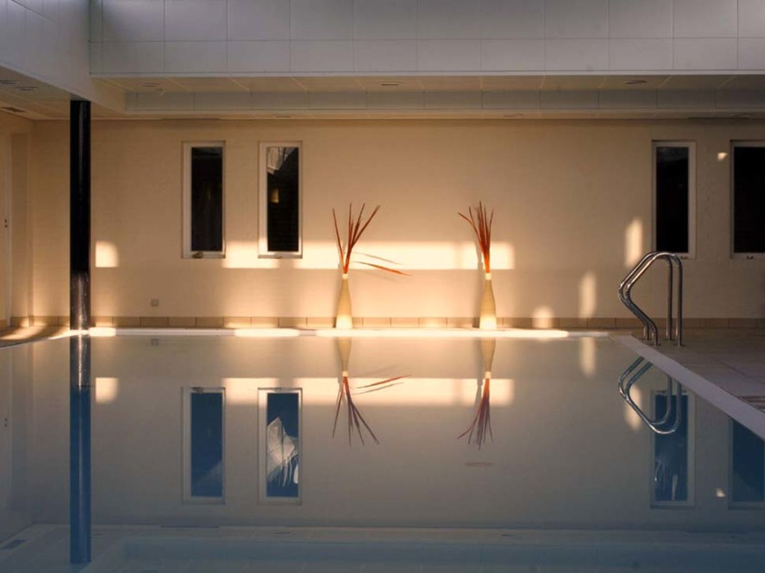 en stor indendørs swimmingpool med mange vinduer og vaser på væggen