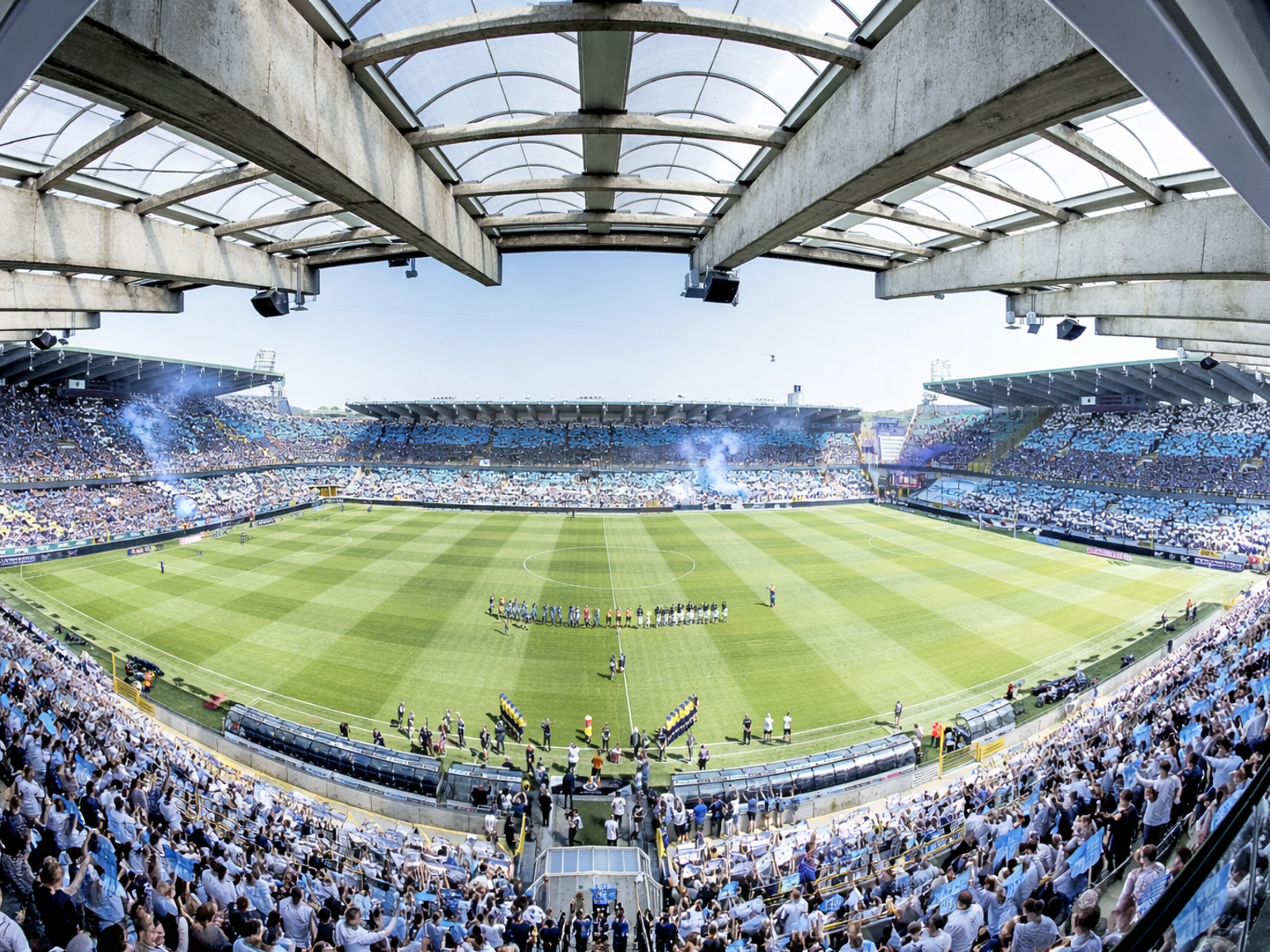 Laajakuva täyteen pakatusta jalkapallostadionista, jossa on sinivalkoisia faneja, sinistä savua ja pelaajia kentällä.