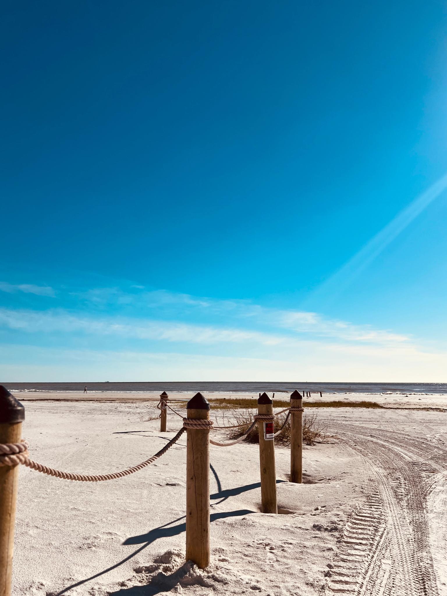 en sandstrand med ett repstaket som leder till havet