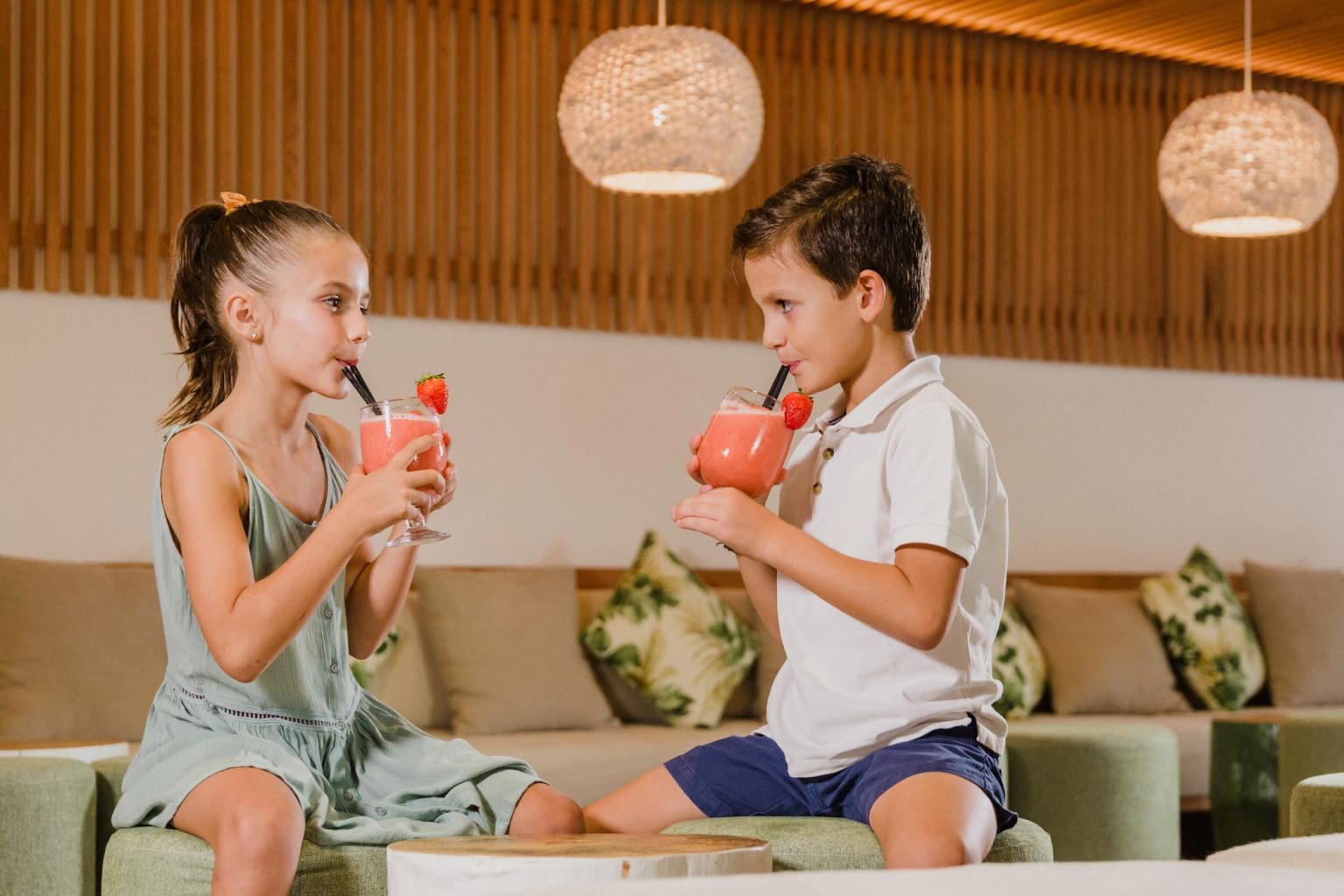 Una niña y un niño beben batidos de fresa en un salón moderno. Aparthotel Club del Sol Resort & SPA