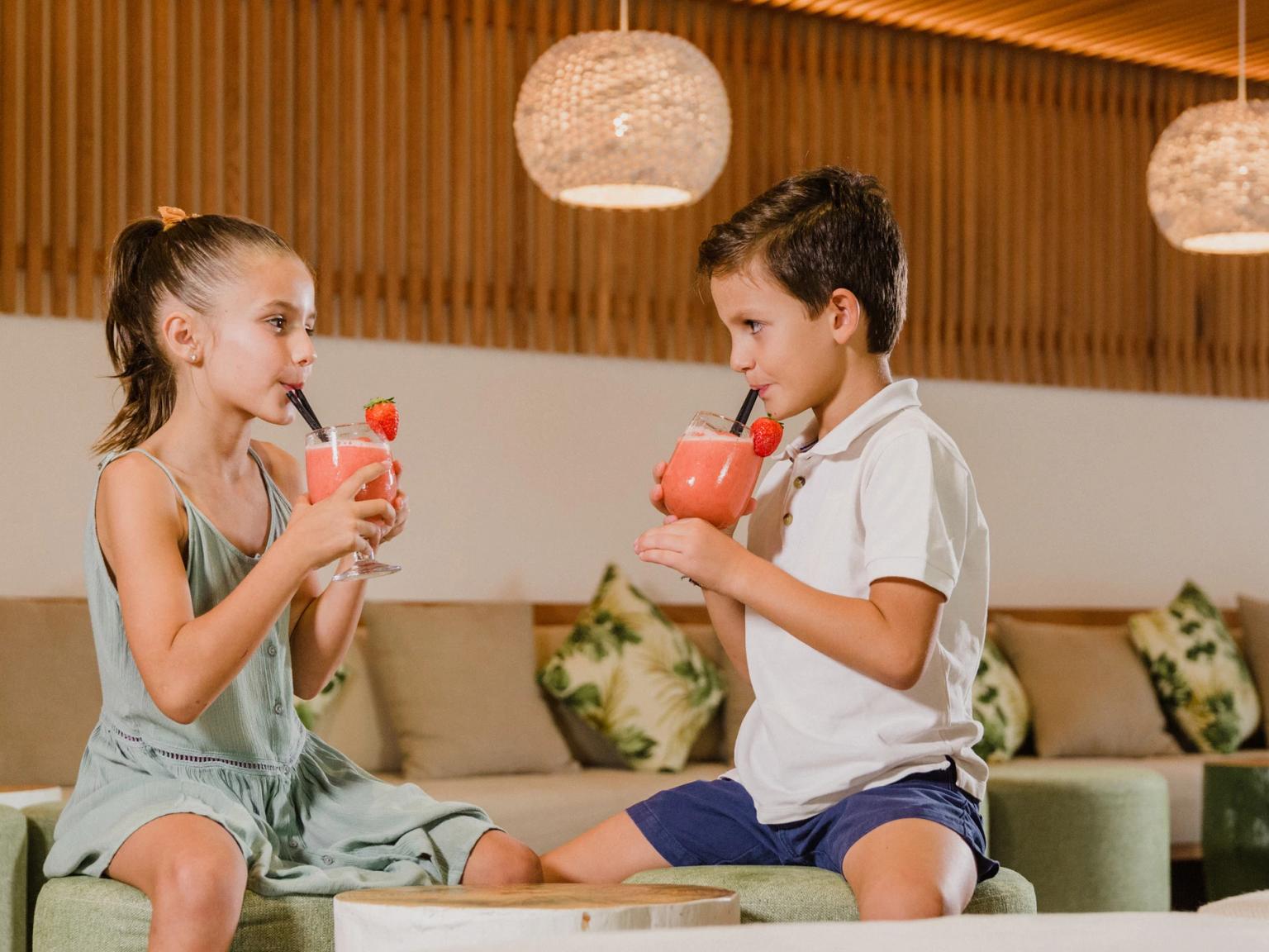 En flicka och en pojke dricker jordgubbssmoothies i en modern lounge. Aparthotel Club del Sol Resort & SPA