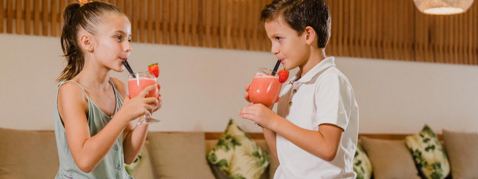 En flicka och en pojke dricker jordgubbssmoothies i en modern lounge. Aparthotel Club del Sol Resort & SPA