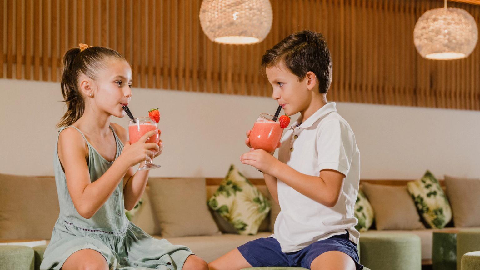 Una niña y un niño beben batidos de fresa en un salón moderno. Aparthotel Club del Sol Resort & SPA