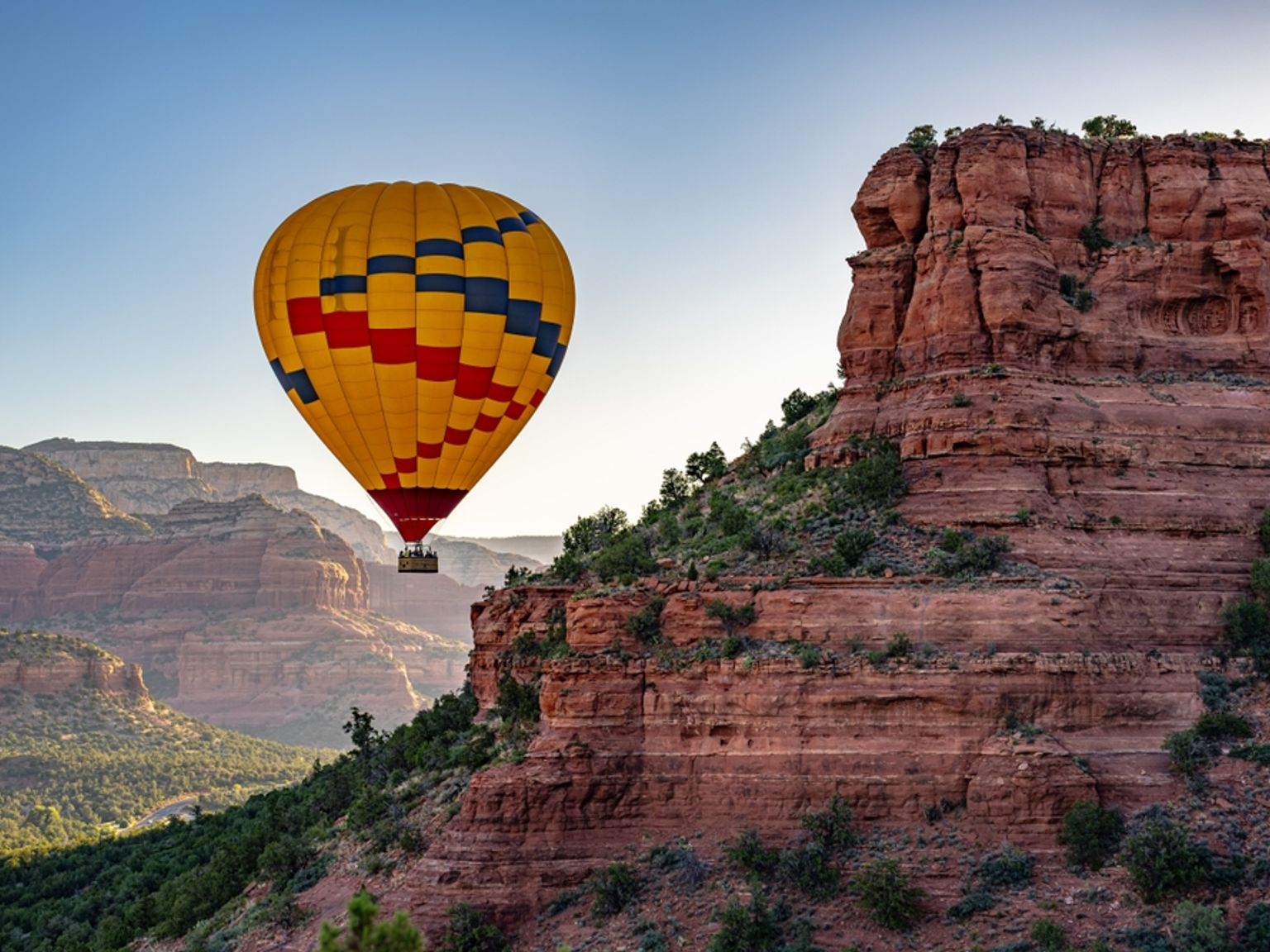 En gul, rød og blå luftballong flyr over røde fjellkløfter. Sedona