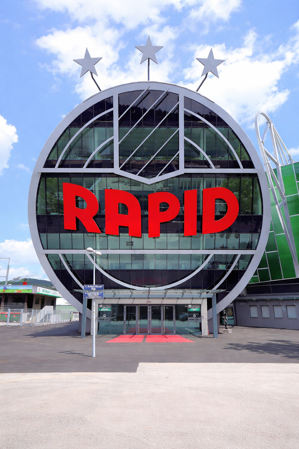 Moderne Gebäude-Eingang mit einer runden Glasfassade, die "RAPID" in Rot anzeigt, gekrönt von drei weißen Sternen.