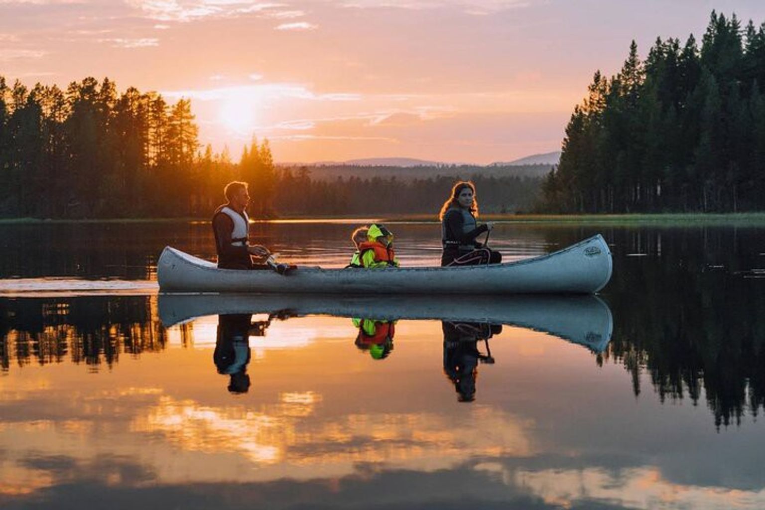 eine Familie rudert ein Kanu auf einem See bei Sonnenuntergang