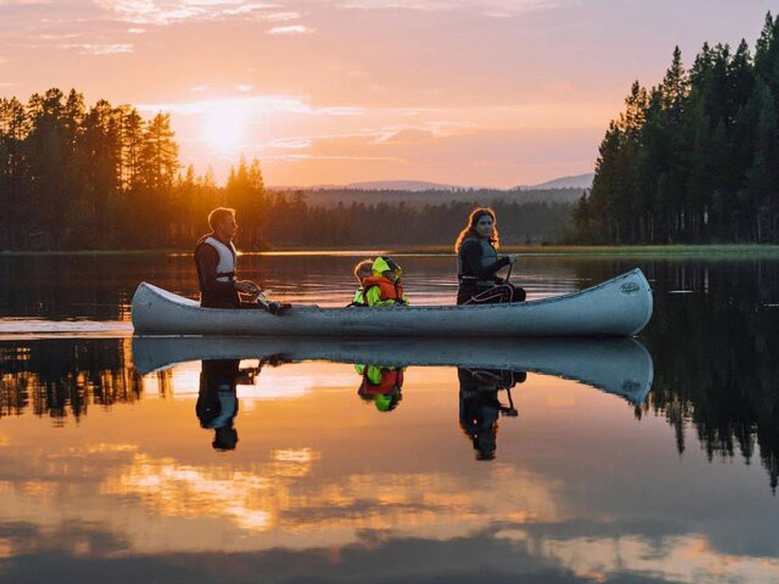 eine Familie rudert ein Kanu auf einem See bei Sonnenuntergang