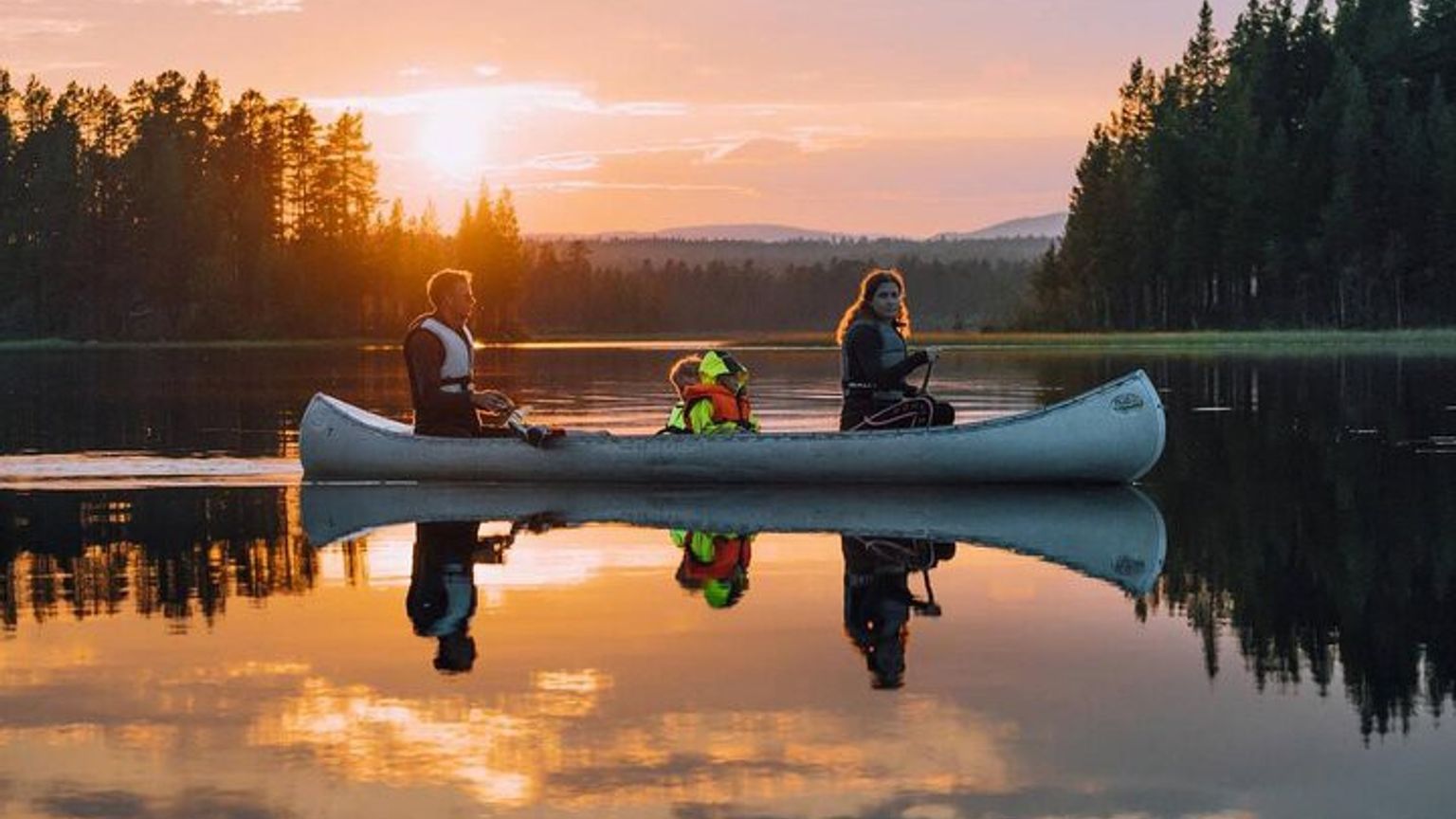 eine Familie rudert ein Kanu auf einem See bei Sonnenuntergang