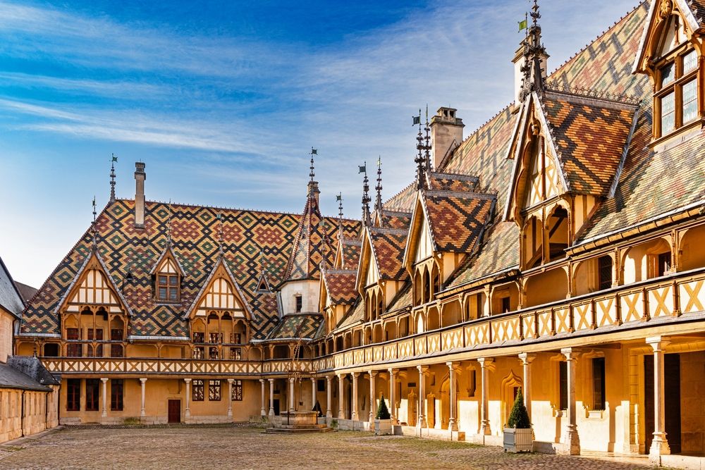 Historic courtyard building with striking multicolored geometric tiled roofs and an arcaded facade. Beaune, France