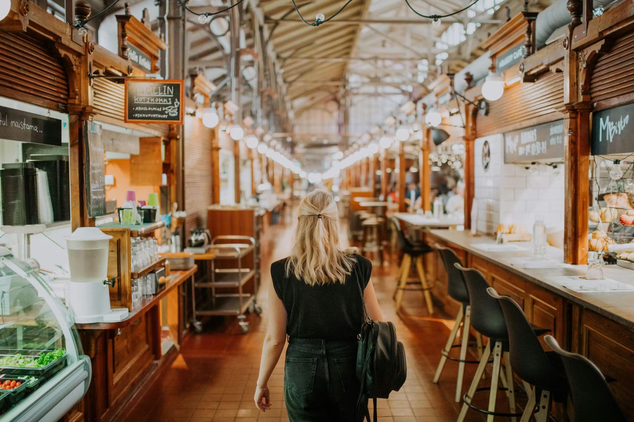 En kvinde går gennem et langt indendørs marked med madboder.