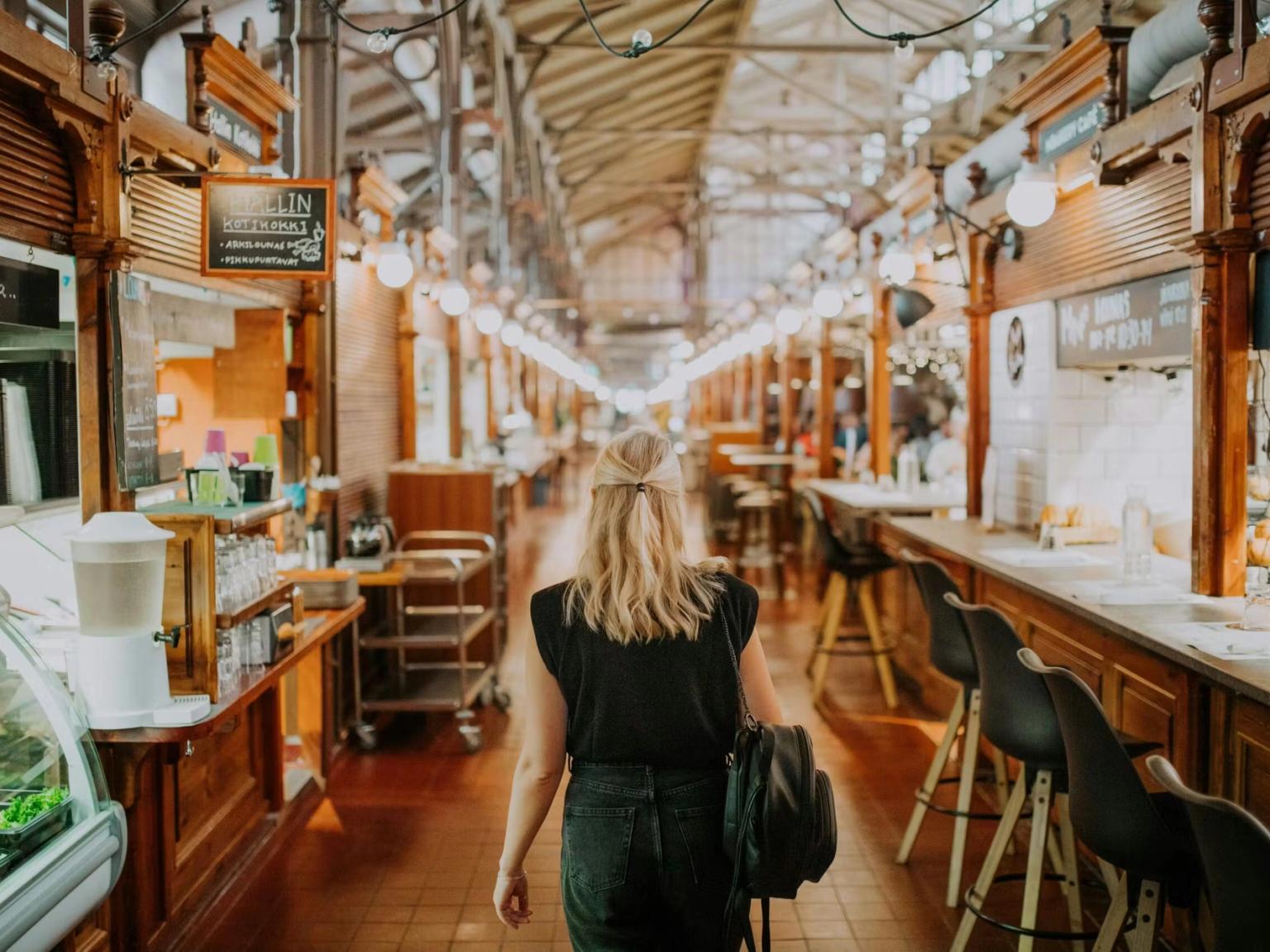 En kvinde går gennem et langt indendørs marked med madboder.