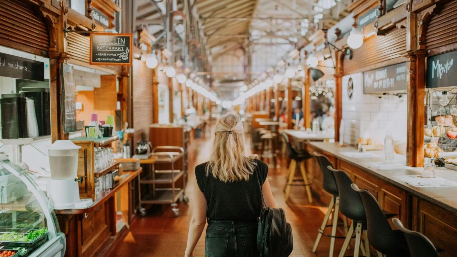 En kvinde går gennem et langt indendørs marked med madboder.