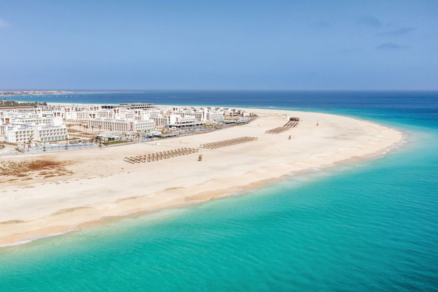 Luftfoto av et feriested på en bred sandstrand med turkist vann.
