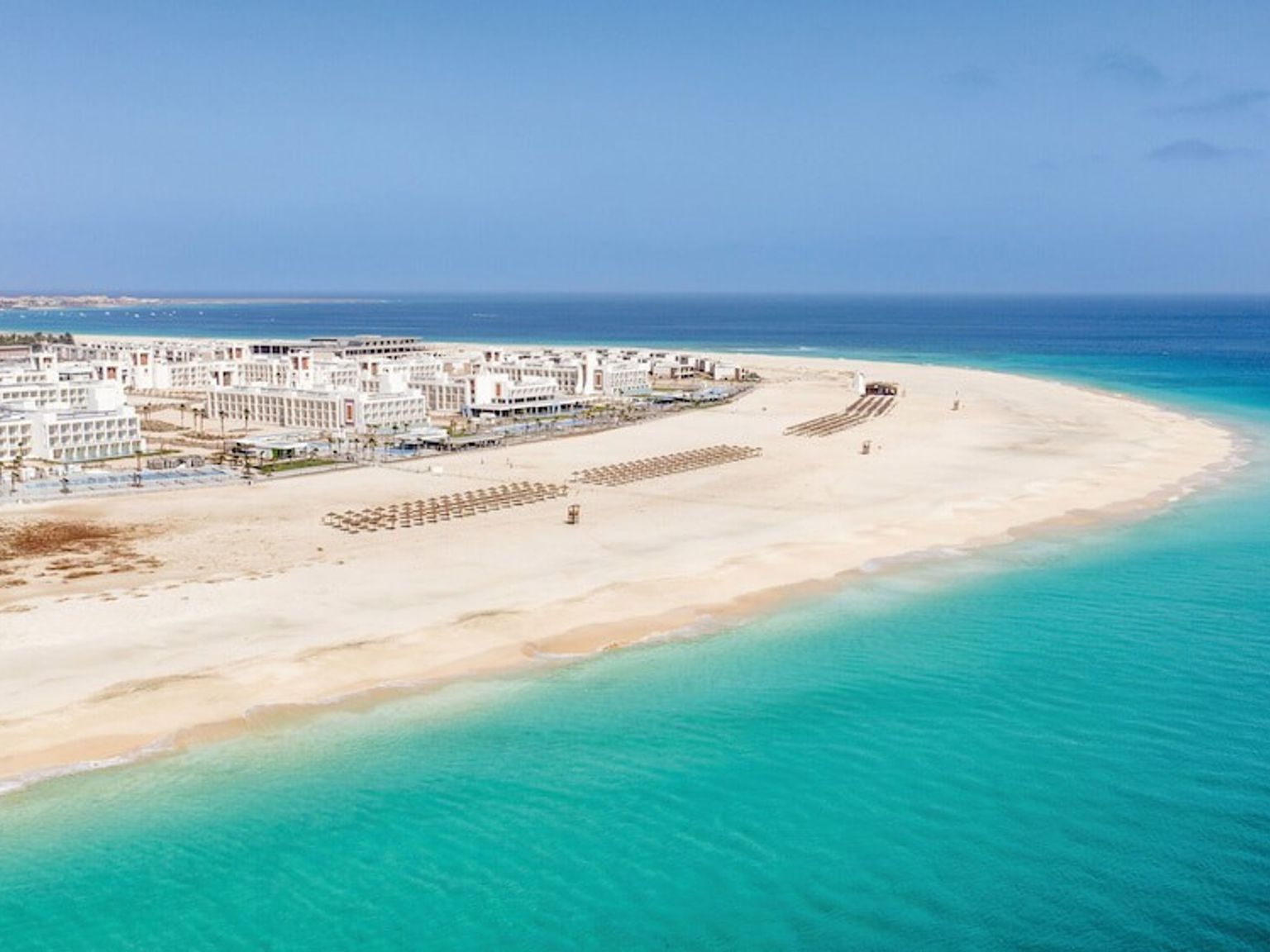 Luftfoto av et feriested på en bred sandstrand med turkist vann.