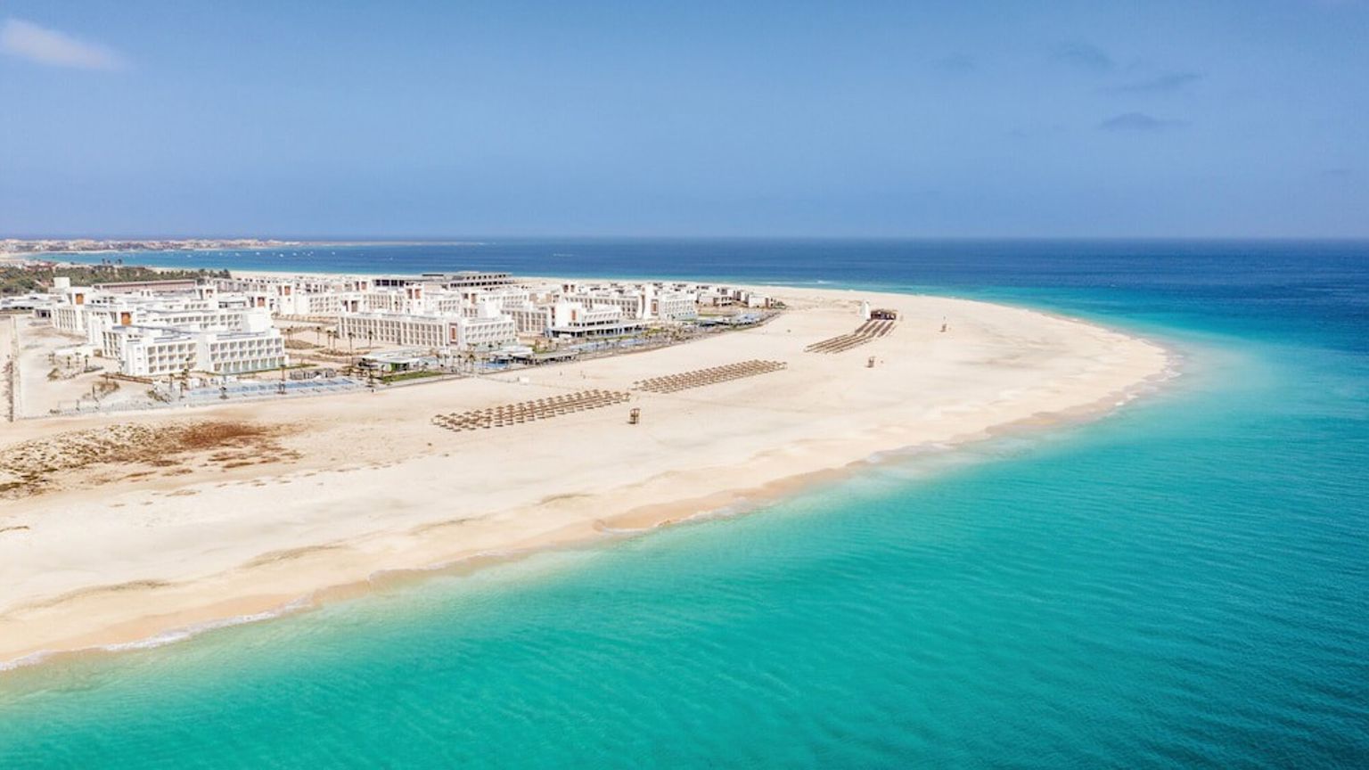 Luftfoto av et feriested på en bred sandstrand med turkist vann.