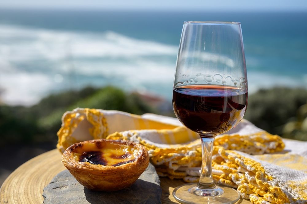 En Pastel de Nata och ett glas rött vin med havet i bakgrunden.