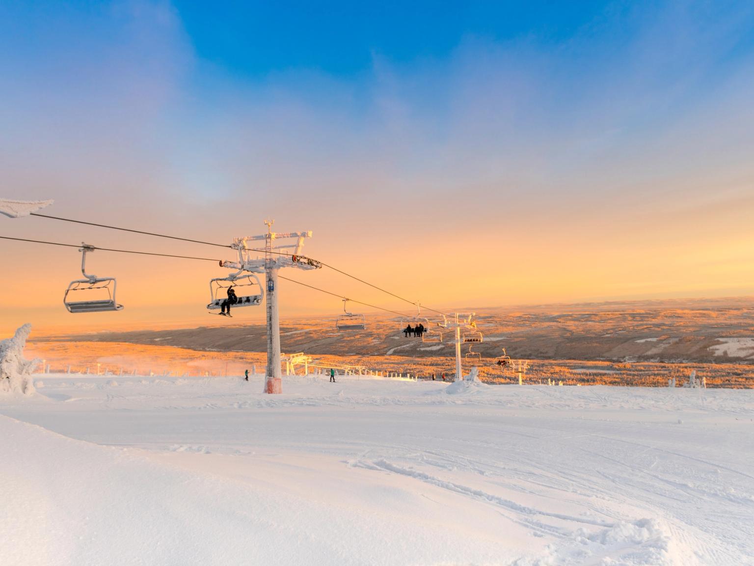 wyciąg narciarski przewożący ludzi na pokrytym śniegiem stoku o zachodzie słońca