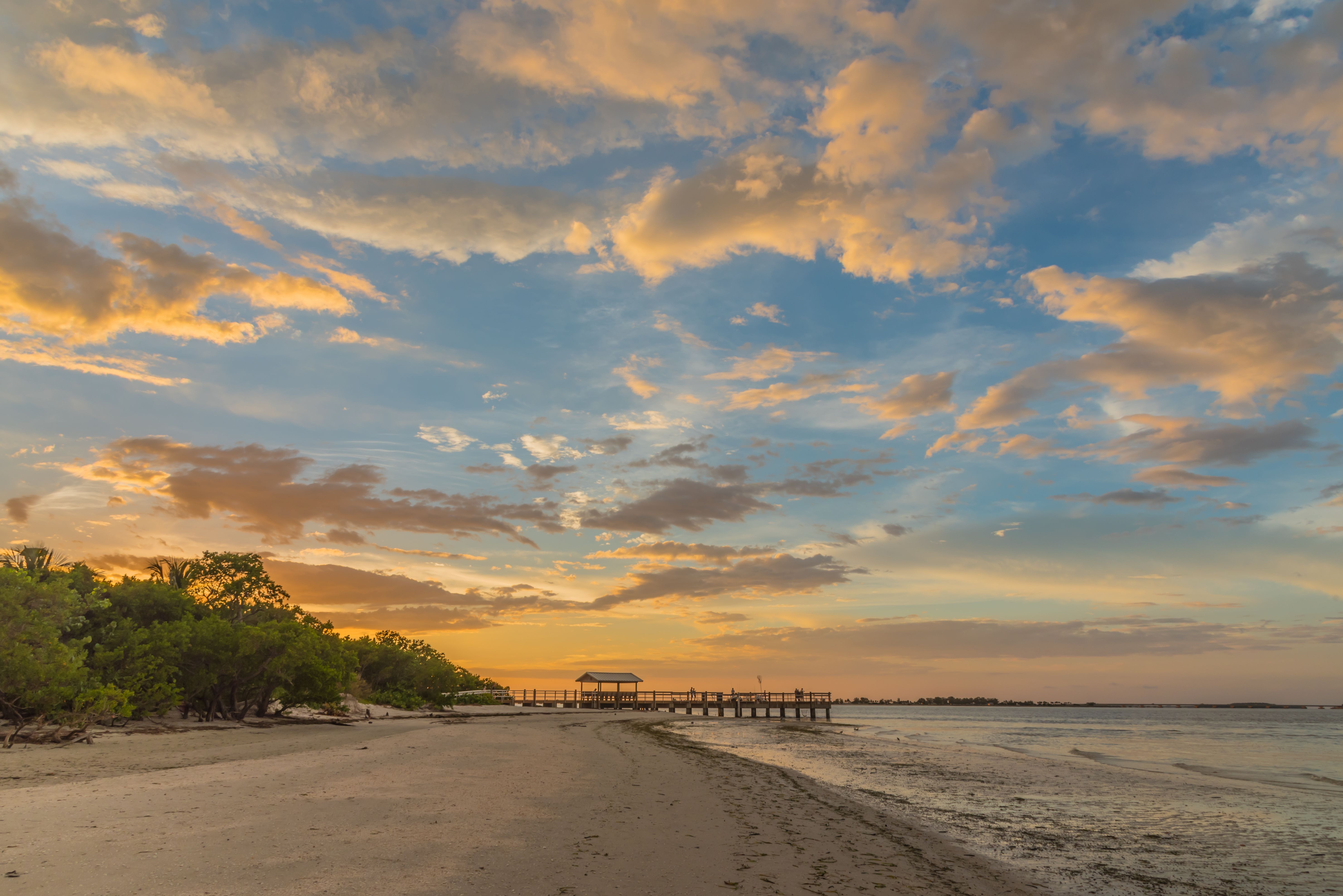 en solnedgang over en strand med en mole i det fjerne
