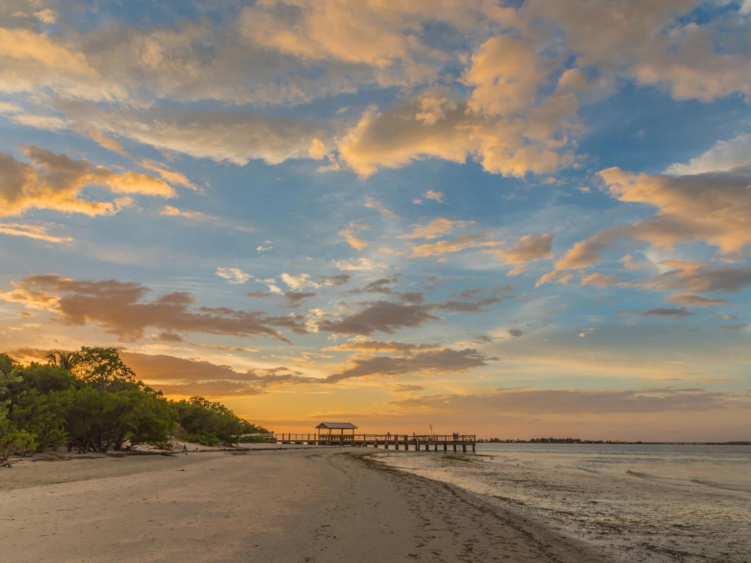 en solnedgang over en strand med en brygge i det fjerne