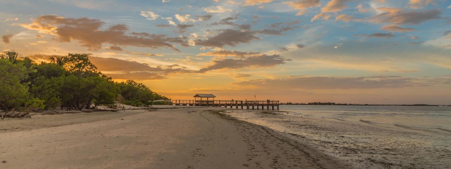 en solnedgang over en strand med en brygge i det fjerne