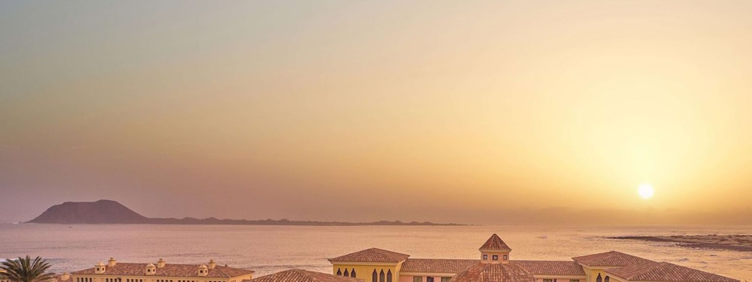 en luftvisning af en stor bygning med palmetræer foran havet ved solnedgang