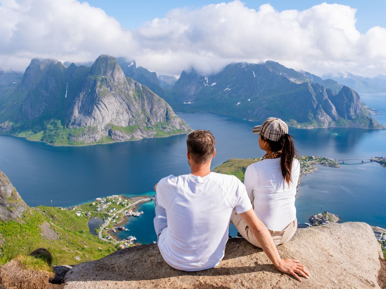 ein Mann und eine Frau sitzen auf einem Berggipfel mit Blick auf das Meer
