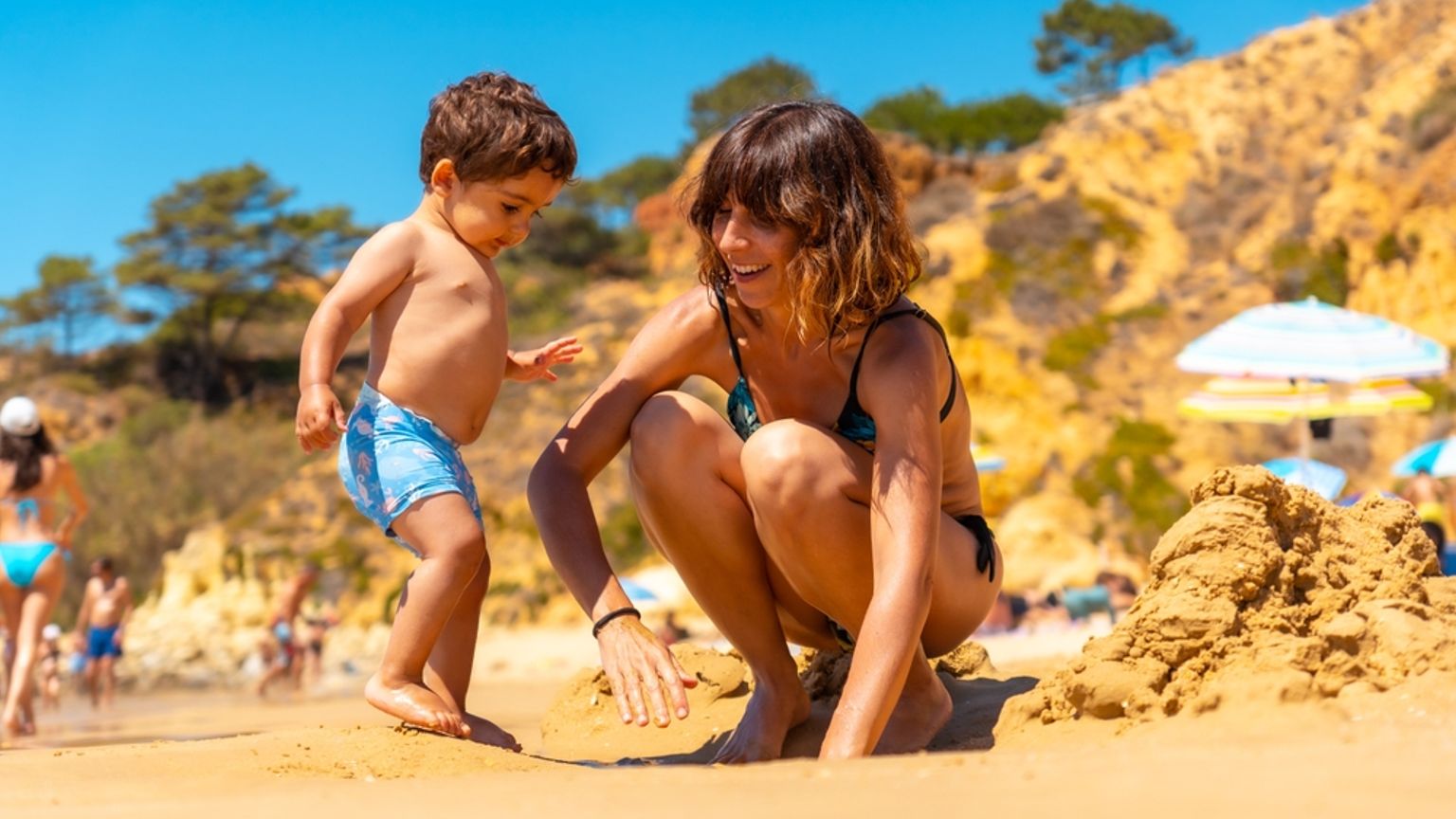 En mamma och ett litet barn leker med sand på en solig strand.