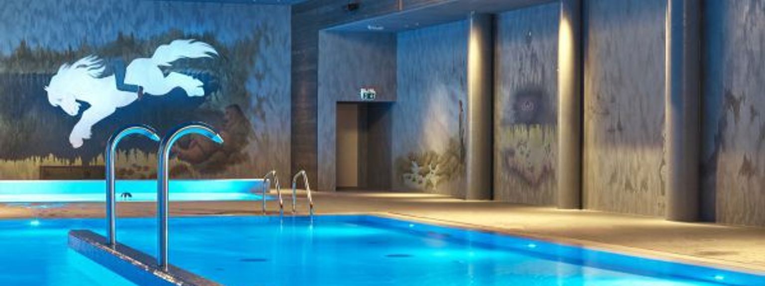 en stor indendørs swimmingpool med blåt vand og en mural på væggen