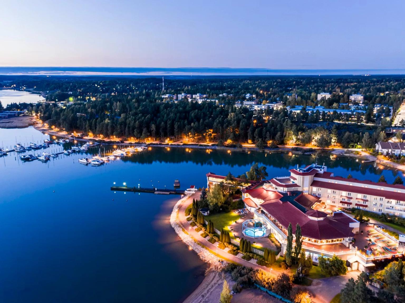 Luftfoto af et klart oplyst feriekompleks og en marina ved en sø i skumringen.