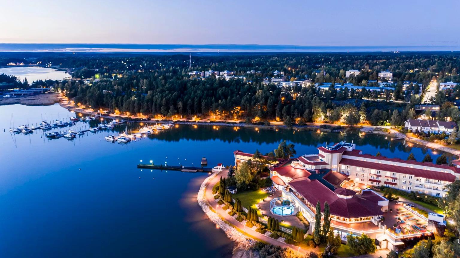 Luftfoto af et klart oplyst feriekompleks og en marina ved en sø i skumringen.