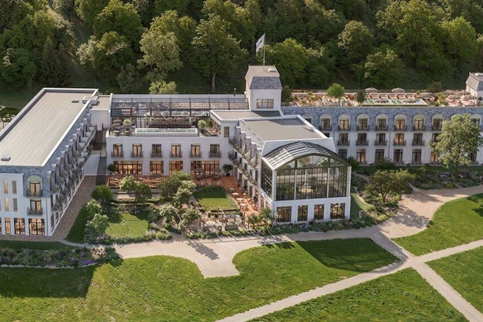 Elegant vitt hotell med mörka tak, omgivet av frodiga trädgårdar och en skog. Rox Resort