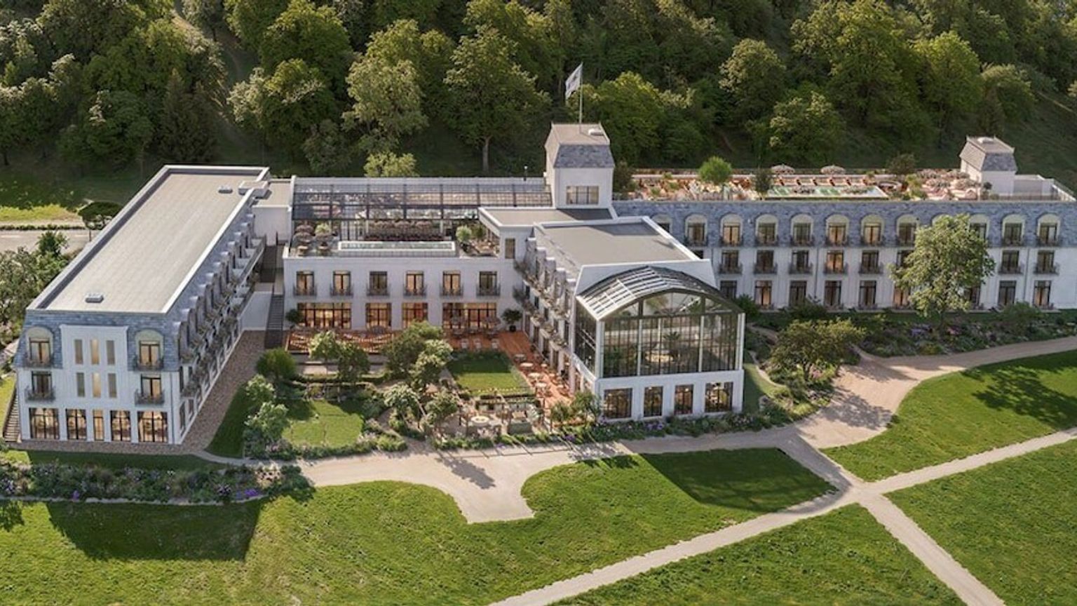 Elegant vitt hotell med mörka tak, omgivet av frodiga trädgårdar och en skog. Rox Resort