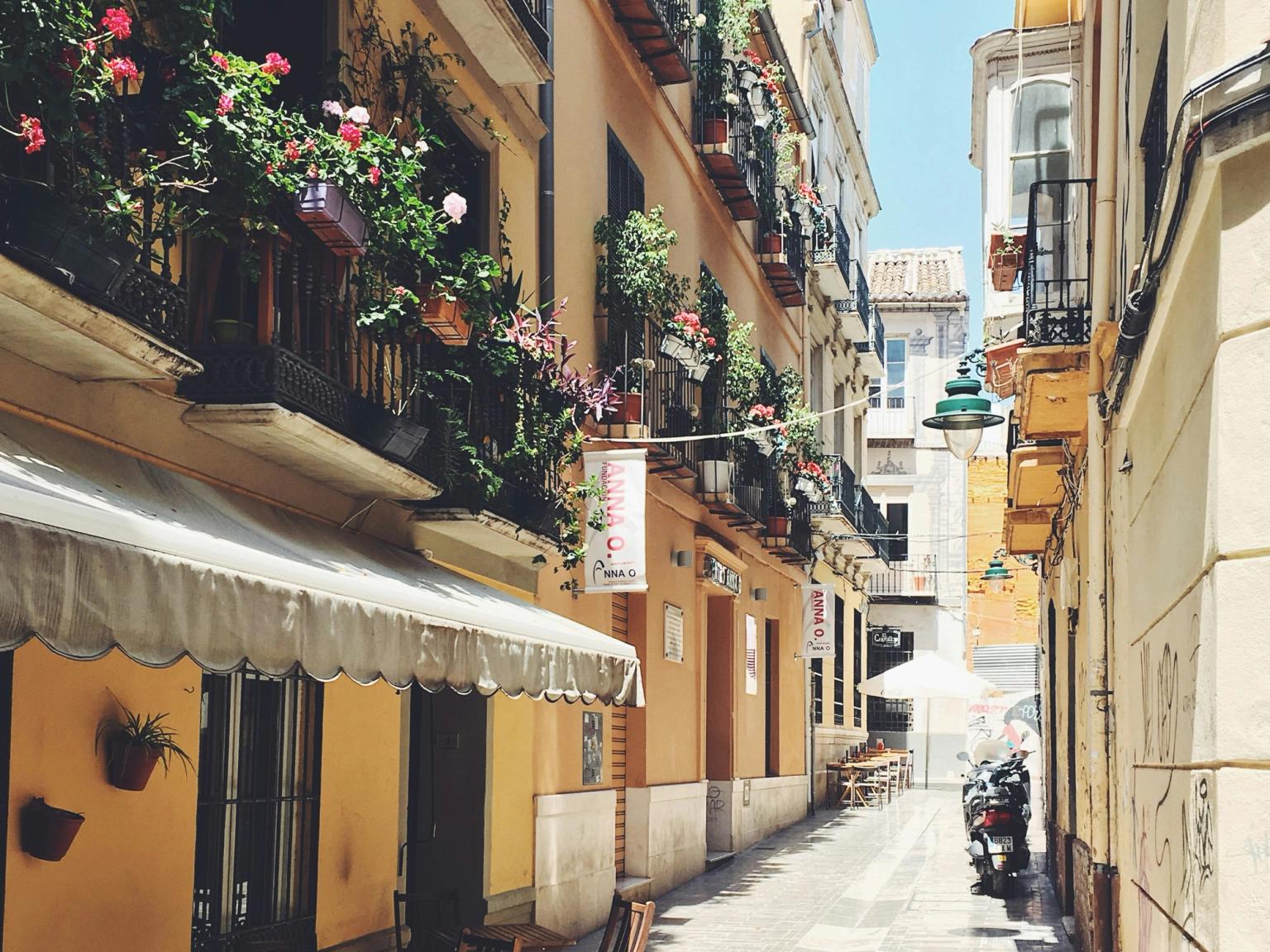 en smal gränd i Malaga mellan två byggnader med blommor på balkongerna