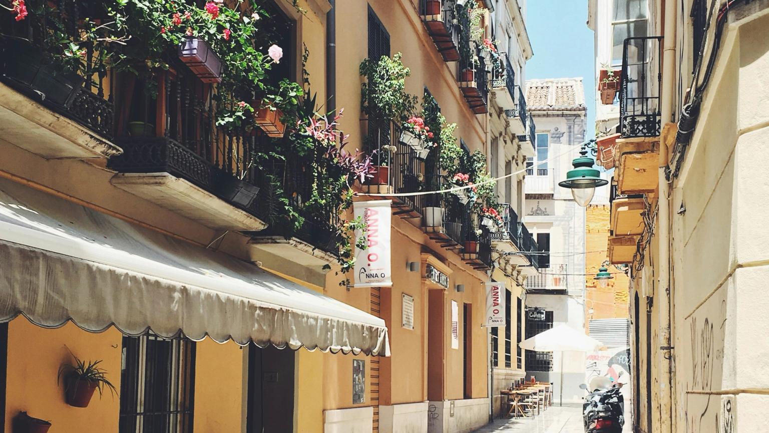 en smal gränd i Malaga mellan två byggnader med blommor på balkongerna