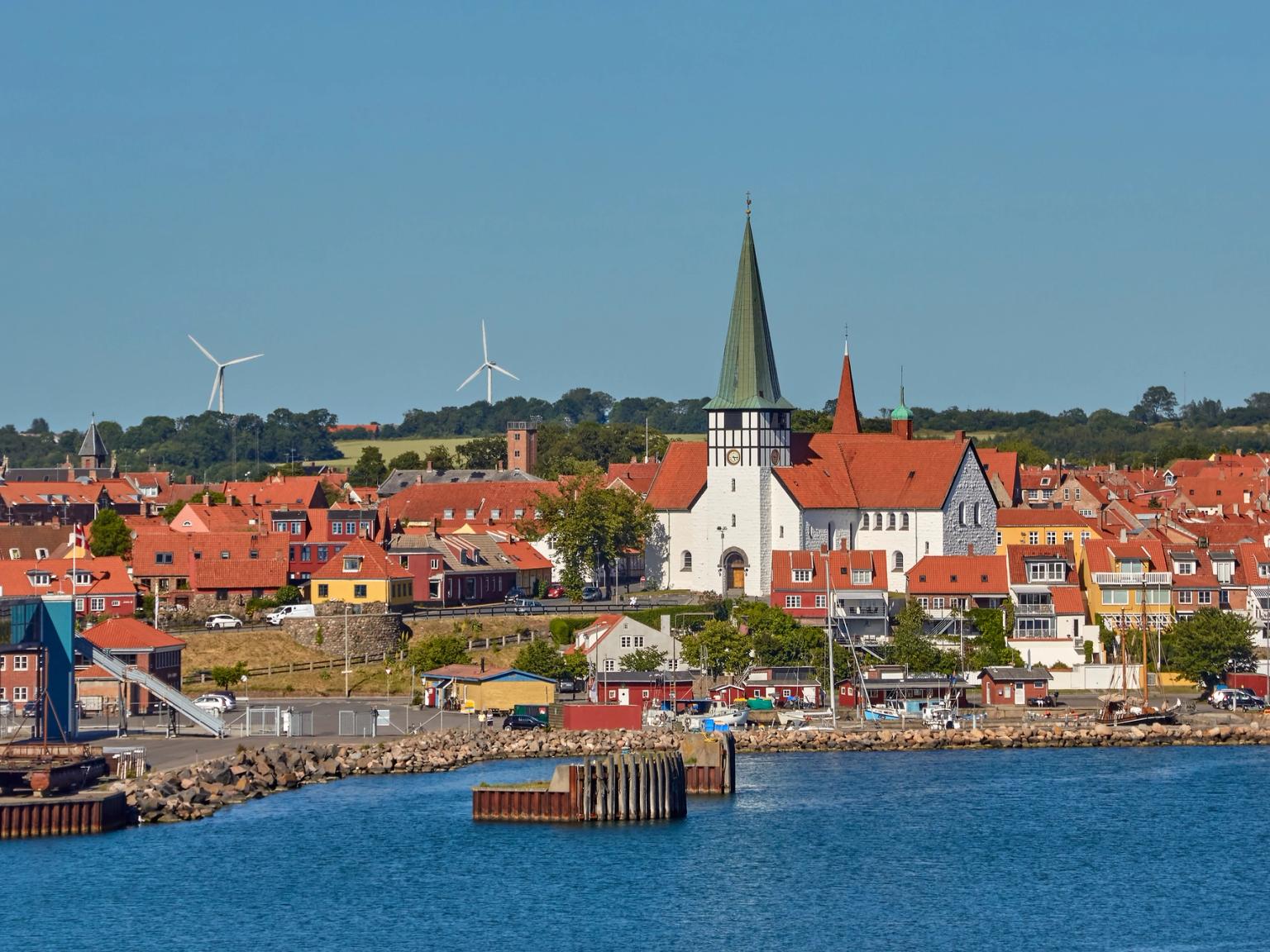 en vy över en stad från vattnet med en kyrka och väderkvarnar i bakgrunden.