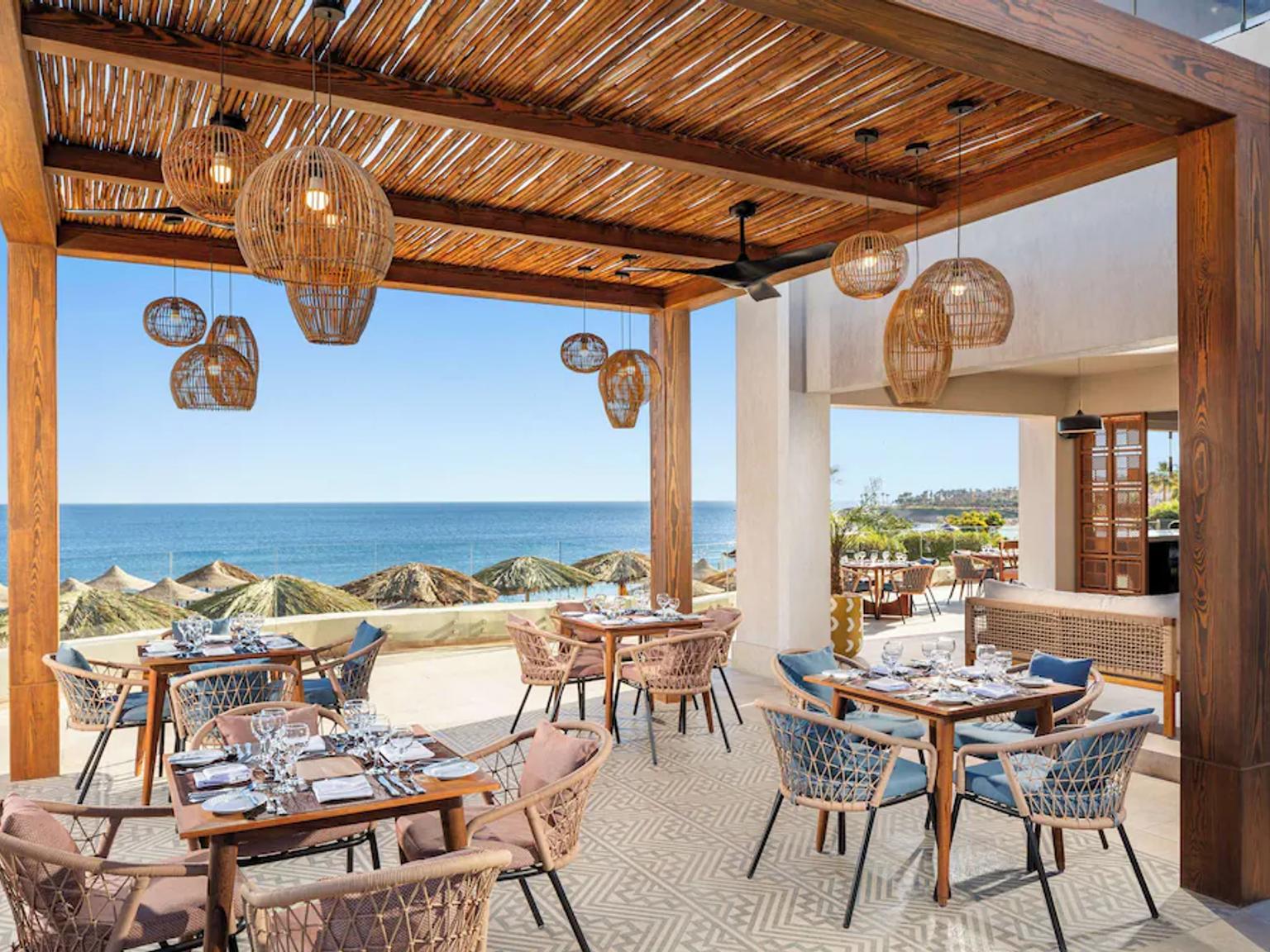 Outdoor beachfront restaurant patio with dining tables and a view of the ocean.