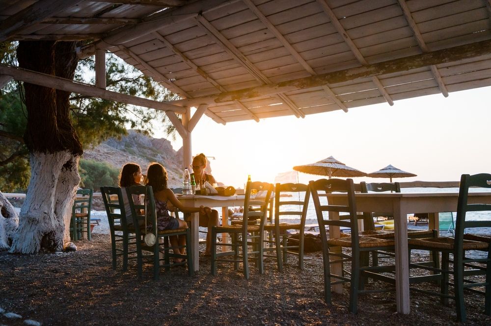 Tre personer äter på en rustik strandtaverna vid solnedgången.