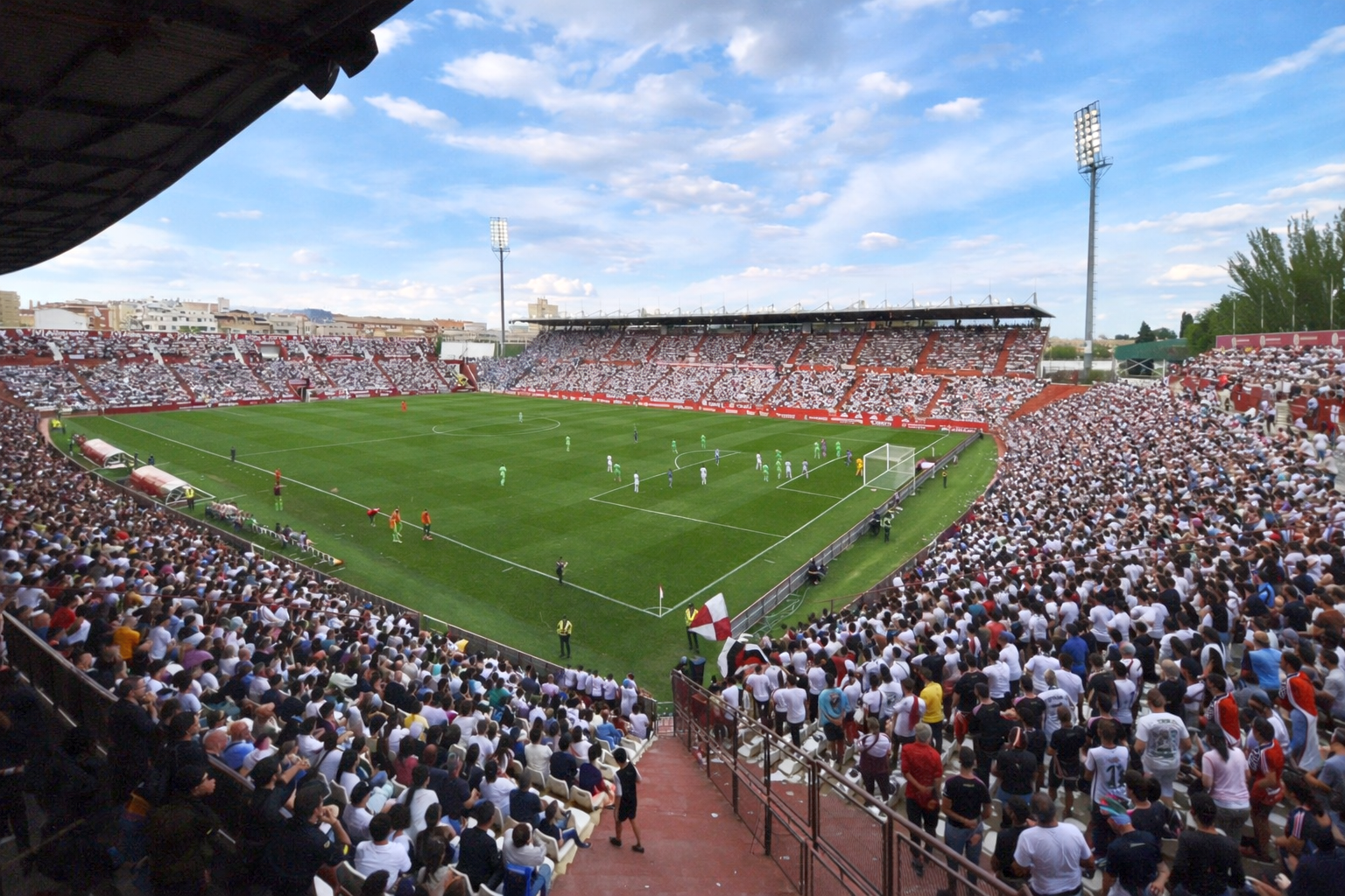 Um grande estádio de futebol lotado de torcedores assistindo a uma partida em campo sob um céu nublado.