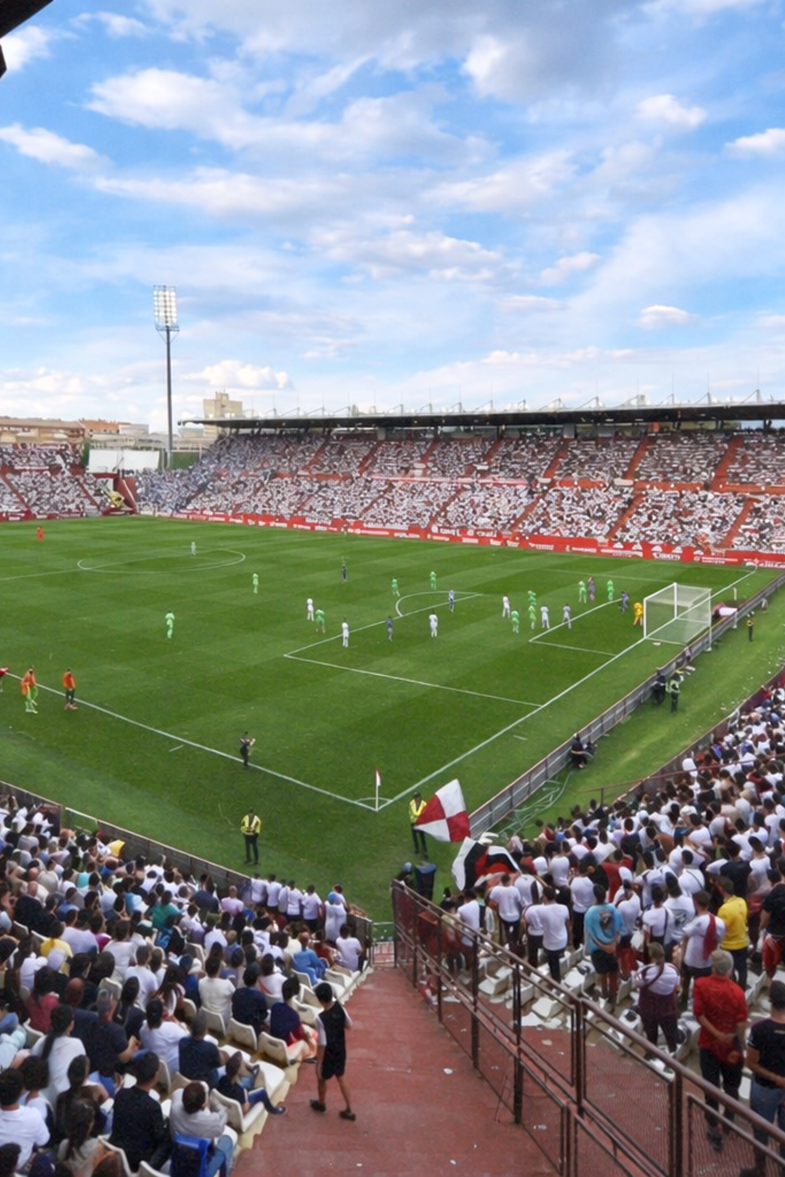 Um grande estádio de futebol lotado de torcedores assistindo a uma partida em campo sob um céu nublado.