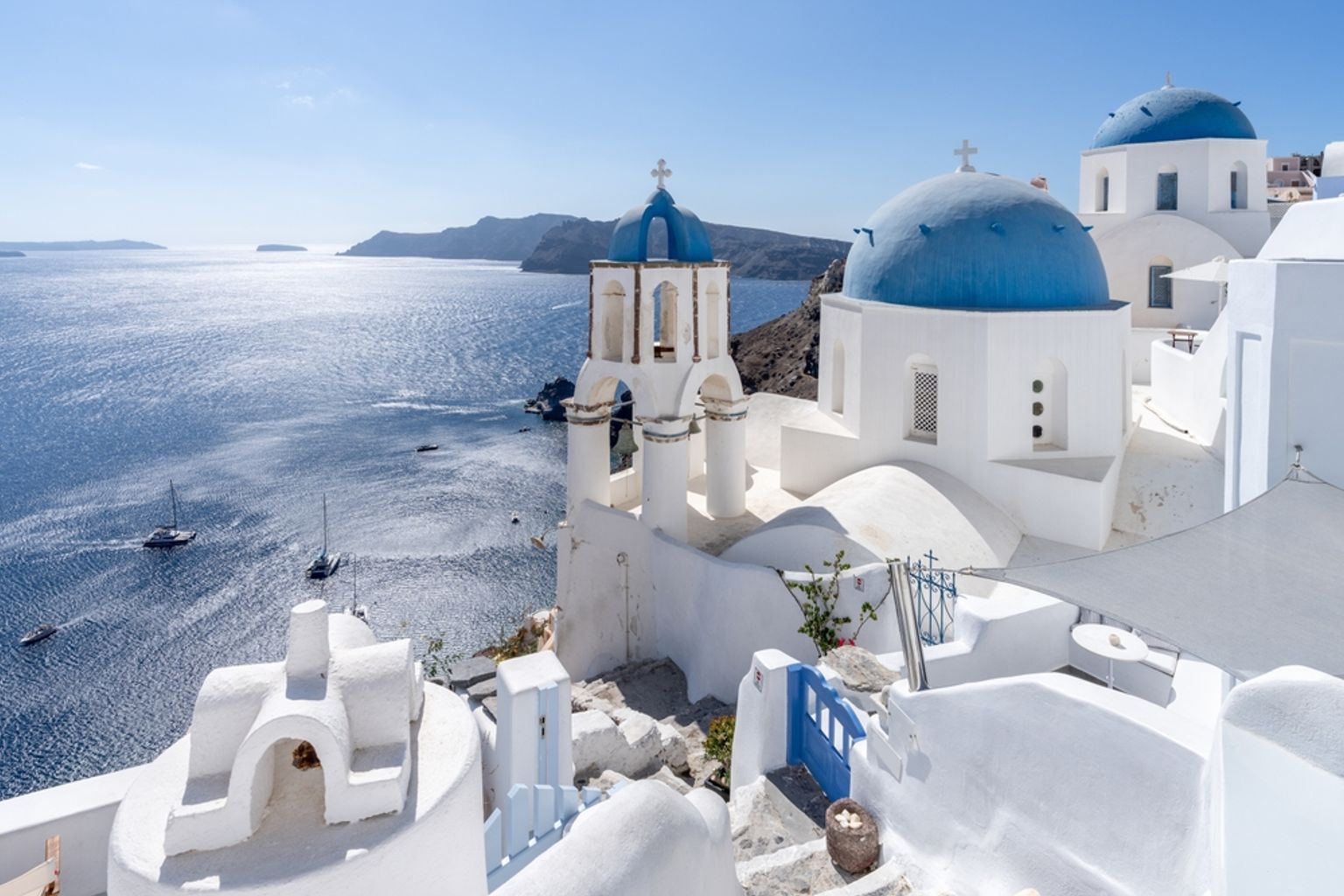 White buildings with blue domes and bell towers overlooking a sparkling blue sea, Santorini, Greece