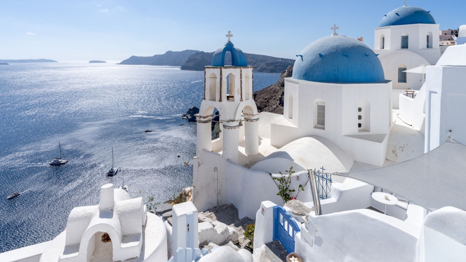 White buildings with blue domes and bell towers overlooking a sparkling blue sea, Santorini, Greece