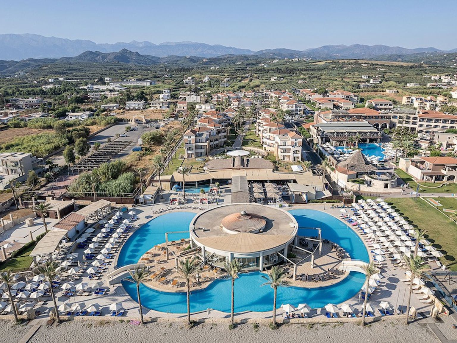 en flygvy över en stor swimmingpool omgiven av palmer och parasoller