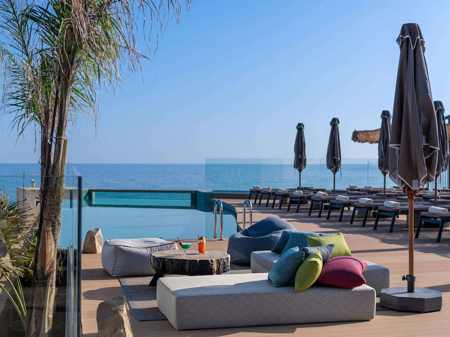 et svømmebasseng omgitt av stoler og parasoller med utsikt over havet.