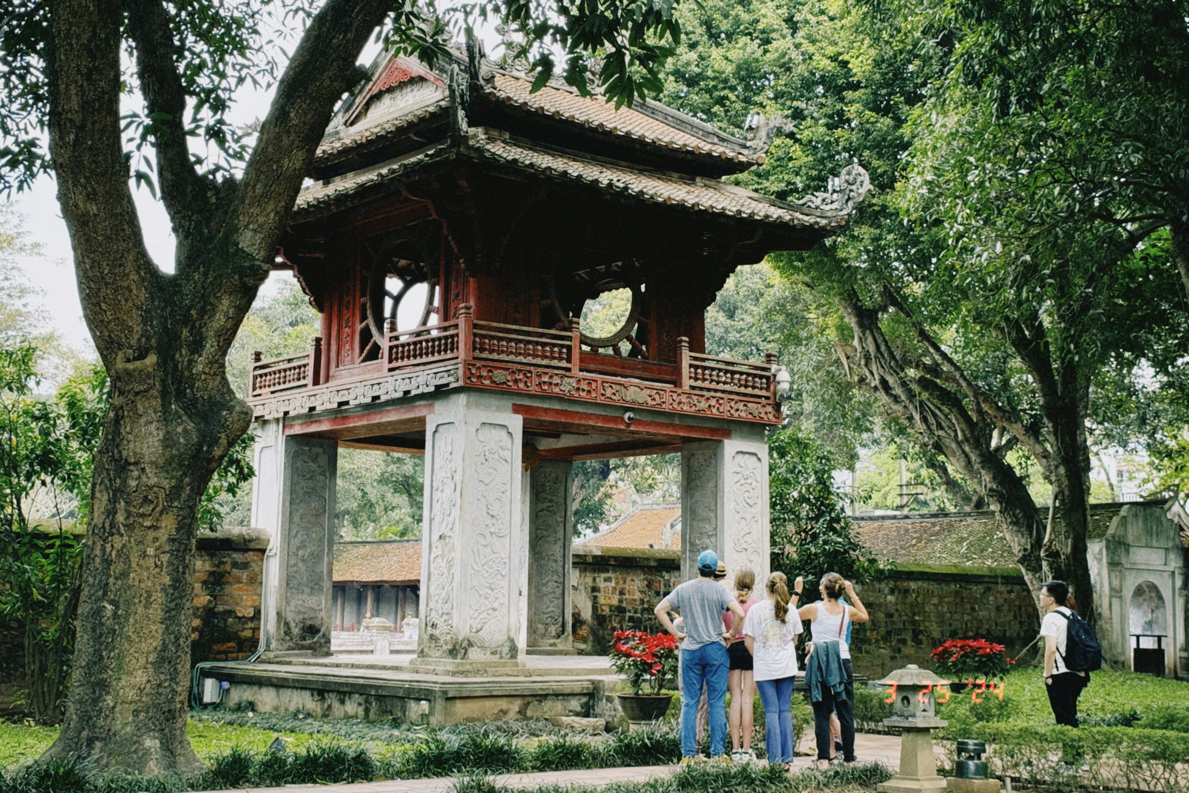 a group of people are standing in front of a pagoda in a park.